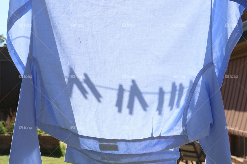 Clothesline and clothespins clothes pegs shadows on hanging shirt on laundry line outdoors on sunny day 