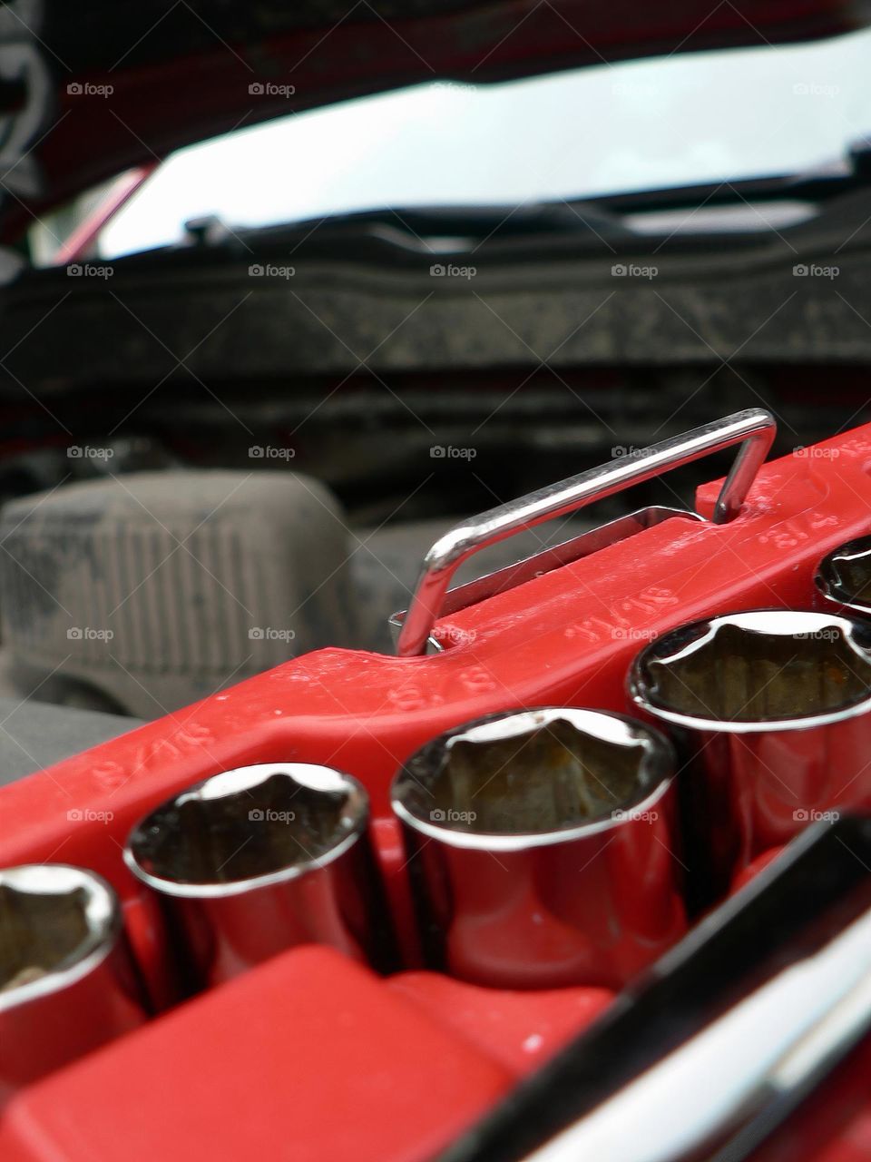 Under the hood of a red pickup truck with combination wrench set tools organized in a red tool hard case by the work station close-up.