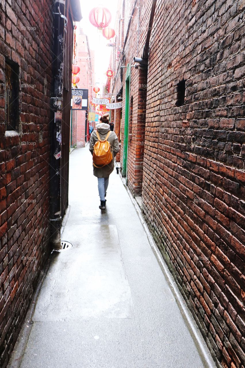 Tourist wandering into the alley surrounded with brick wall