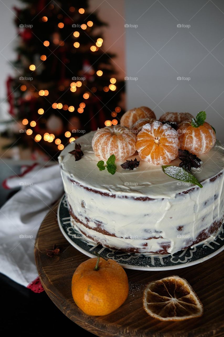 Christmas cake with tangerins on top and a Christmas tree in the background 