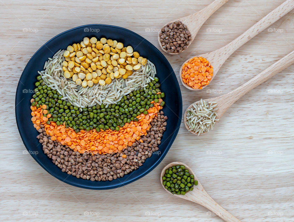 Different grains in the round bowl and in wooden spoons. Rice, moong beans, dal and buckwheat.