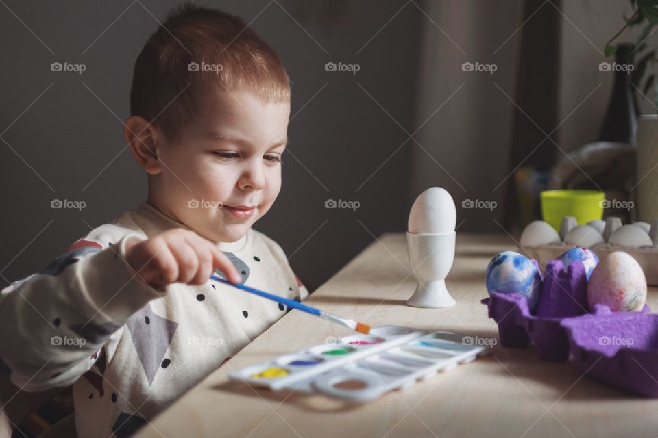 Toddler boy coloring an easter egg with paint