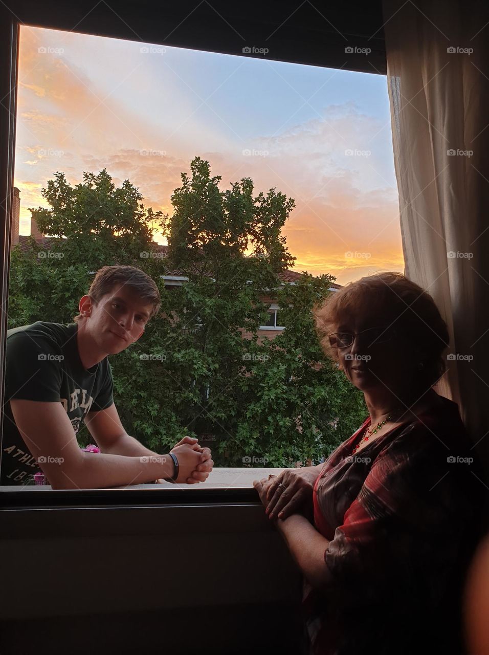 grandmother with her grandson watching the sunset from her window