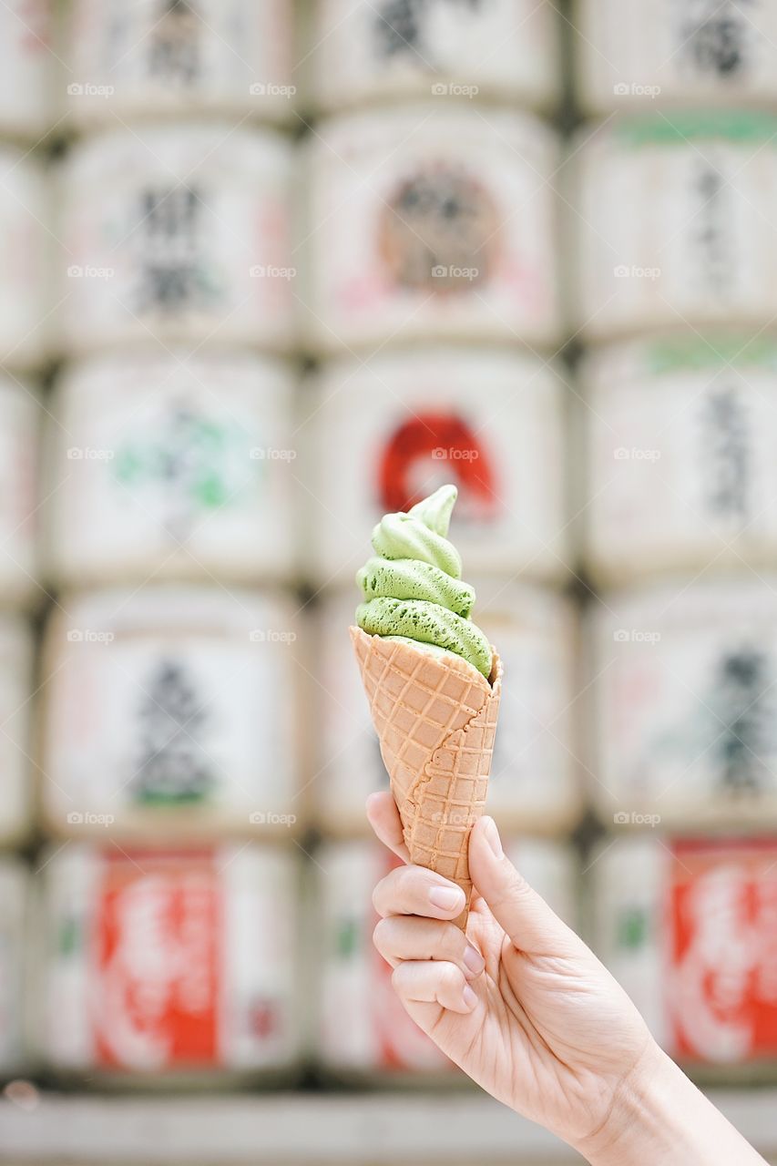 Ice cream cone. A lady’s hand holding Japanese matcha green tea ice cream cone with abstract blur of sake barrel.