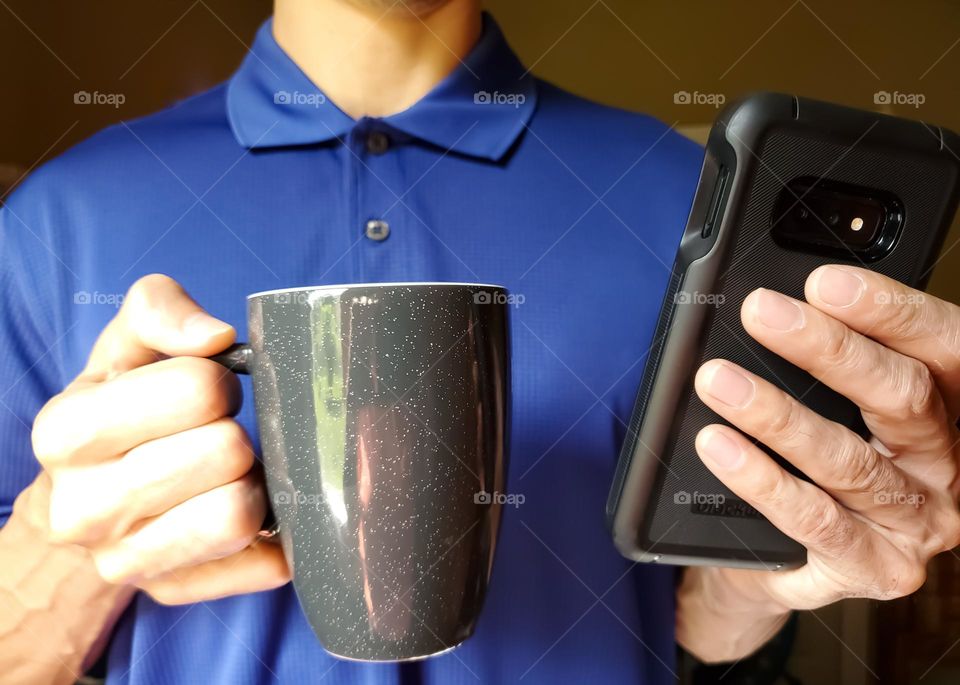 A man drinking coffee while catching up on his cell phone.