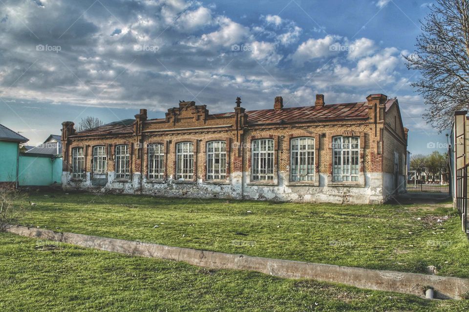 old brick building former garment factory dot blue sky with clouds and green lawn.