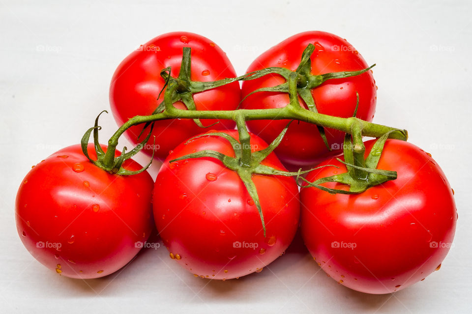 ripe fresh red tomatoes on a green branch, isolated on white background