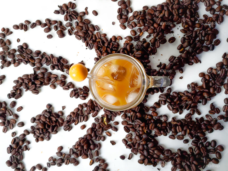 Cold brew ice coffee at home with almond creamer. In a mason jar with a handle. On a white background surrounded by organic whole coffee beans.