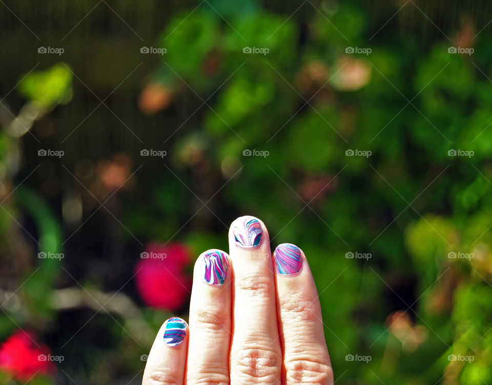 water marble nail art in purple, magenta, bluegreen and white. garden background.