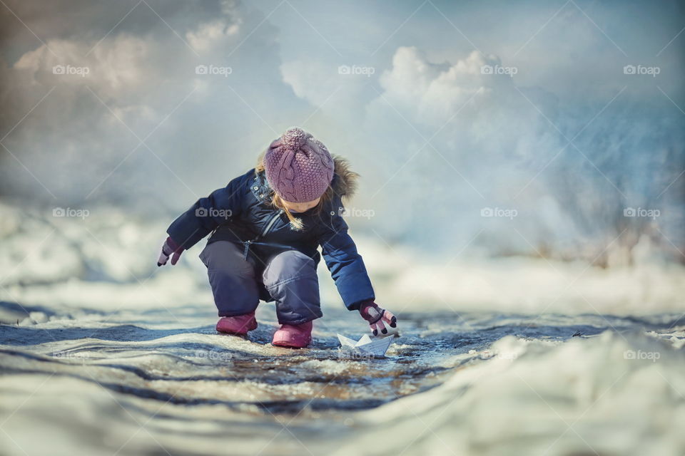 Little girl with paper boat on creek 