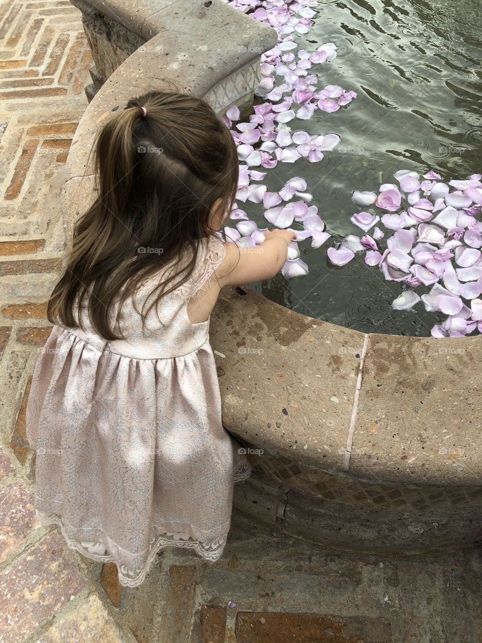 Little girl plays with flower petals in fountain