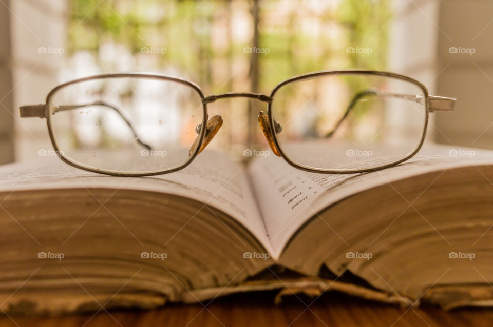 An open book and a specs or eyeglass on wooden table, on a warm sunny morning, side view close up. Education or Holiday Concept. Isolated background in selective focus, shallow depth of field