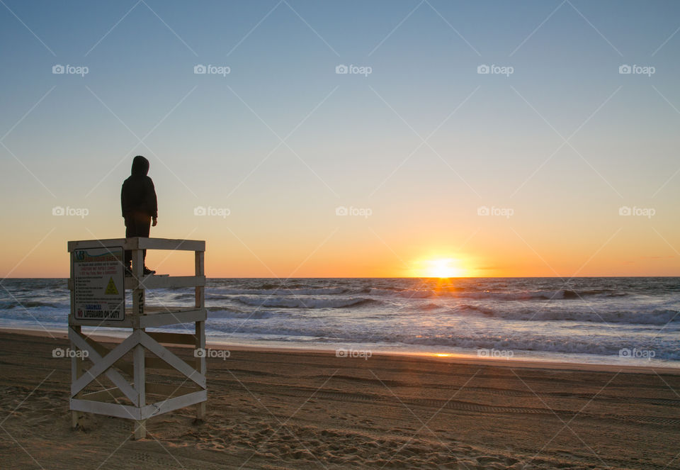 A boy takes in a beach sunrise from a lifeguard chair.