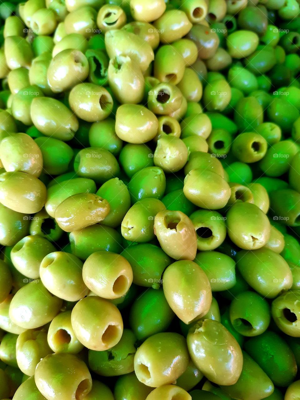 A close-up of fresh, pitted green olives glistening under the light, highlighting their texture and vibrant shades. Captured in Casablanca on January 1, 2025.