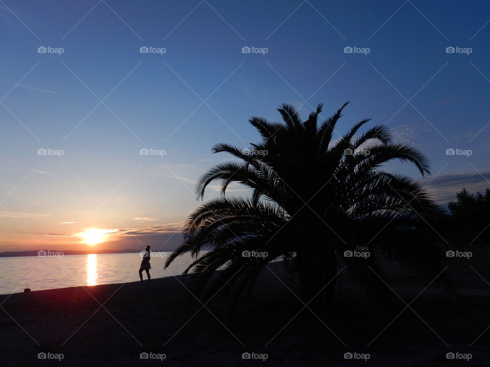 sunset on the beach with girl and palm,blue sky,reflecting sun rays