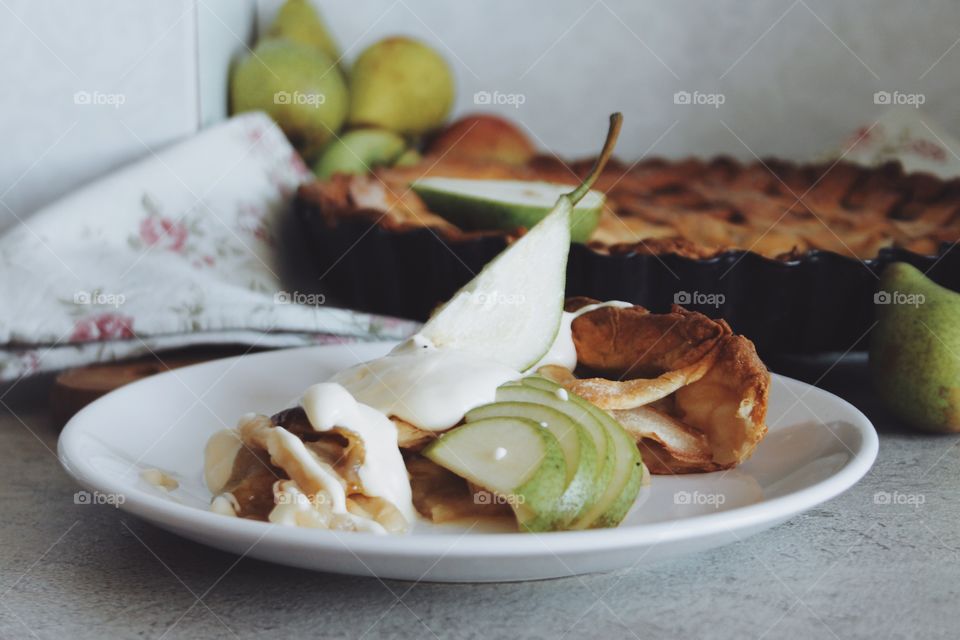 A piece of a pear pie with a cheese cream and a green pear lying on it