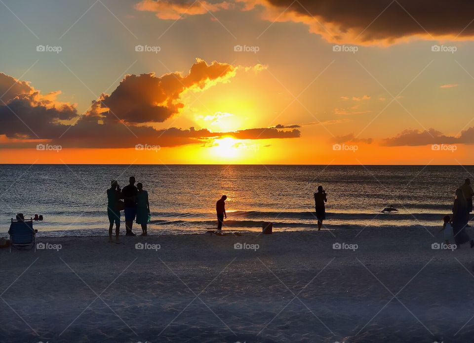 Silhouettes of family and friends on the beach watching the gorgeous golden sun dip into the ocean.