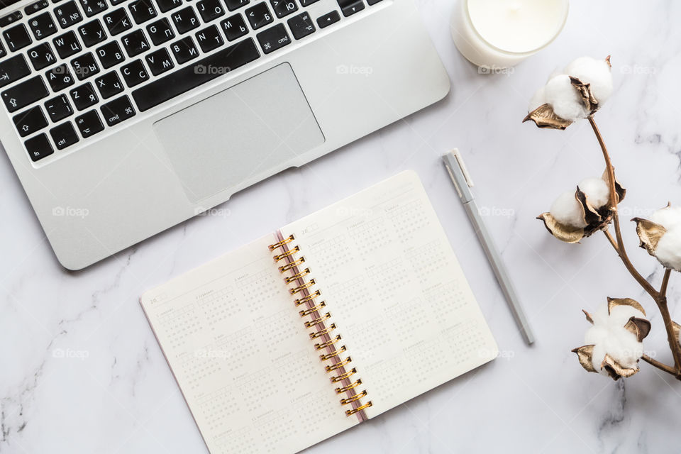 Desktop flatlay items: laptop, calendar, eyeglasses, candle, earrings, pen, cotton flowers lying on marble background 