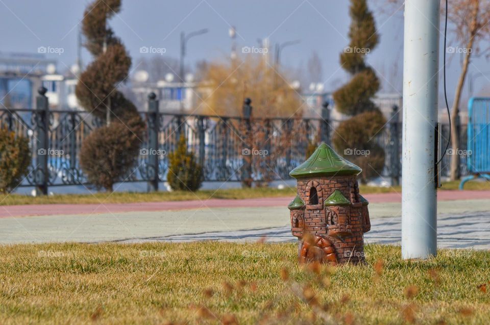 fairy house on the lawn in the city against the background of a fence and two decorative thujas