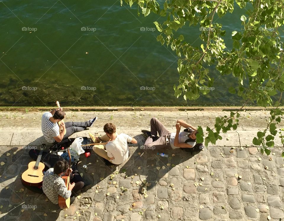 Group of friends playing guitars and having fun together next to a river on spring summer time 