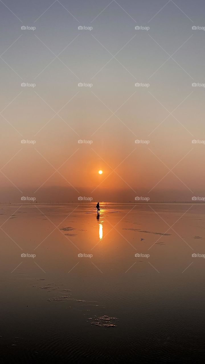 Fisherman during sunrise picking up clams on the beach 