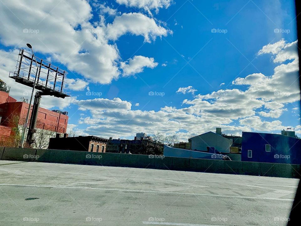 Zooming by in a speeding car we photographed this lovely white cloud pattern in an otherwise clear blue sky. Everything in this image seems to be moving: Clouds, sky, the dark silhouettes of New York City buildings … 2021. Hypnotic Productions 