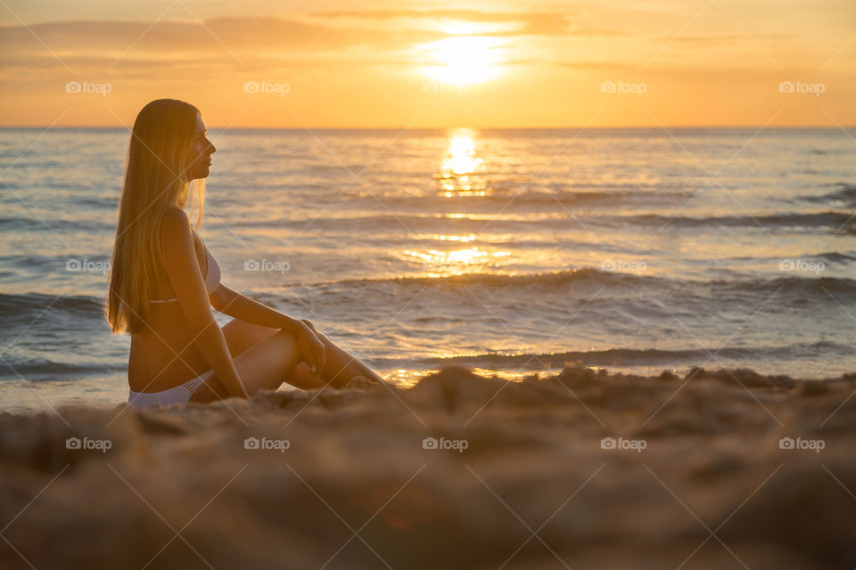 Woman sitting on the sandy beach on sunset 