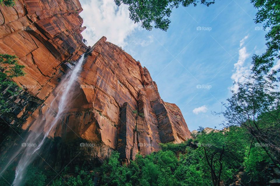 A magnificent low-angle shot of a red rock face with a cascading waterfall.