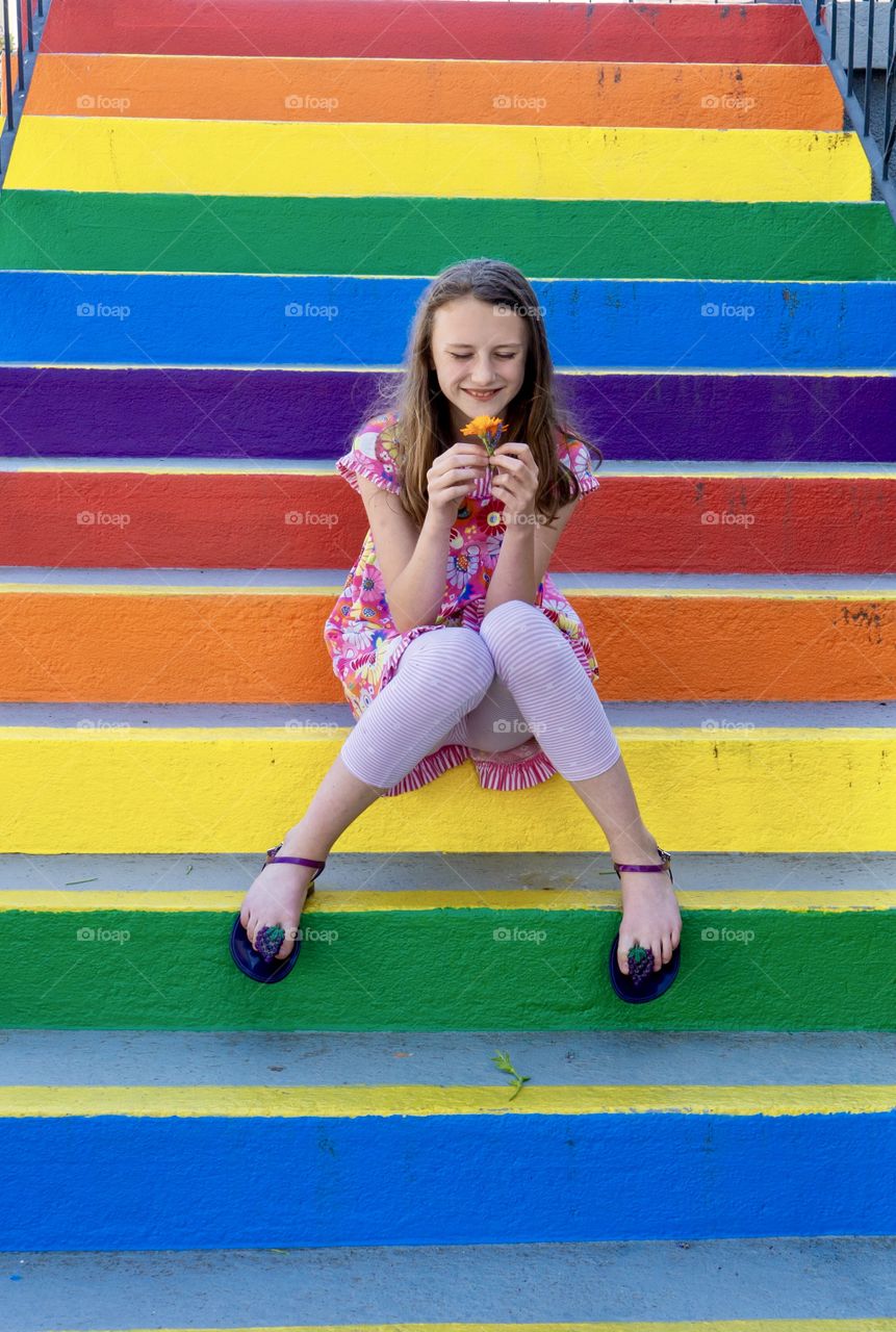 Girl holds orange flower on multi-coloured stairs