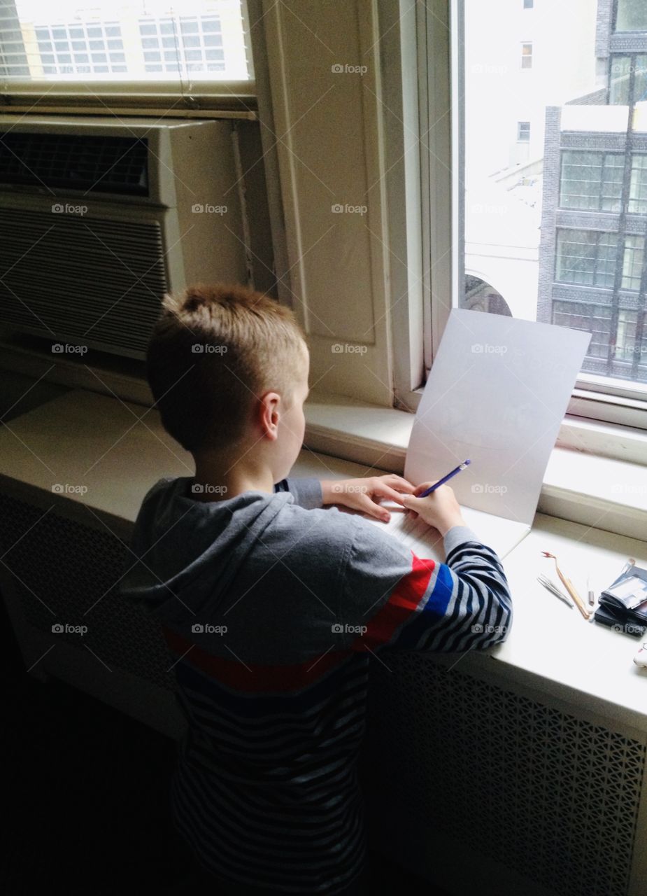 Young man kneeling down doing what he loves working on his drawing looking through window in New York City building. 
