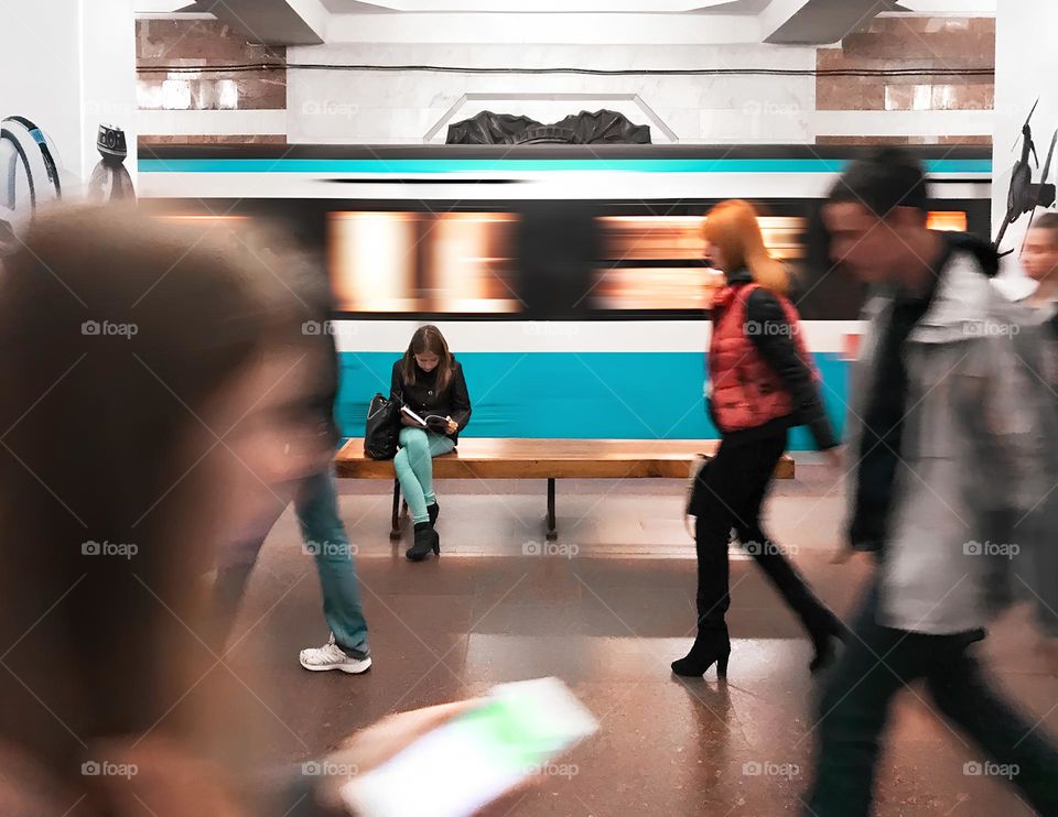 Young woman reading a book in front of moving subway train 