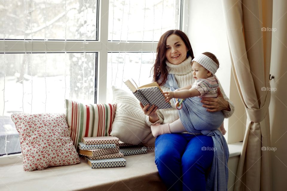 Mother and daughter in baby carrier reading books 