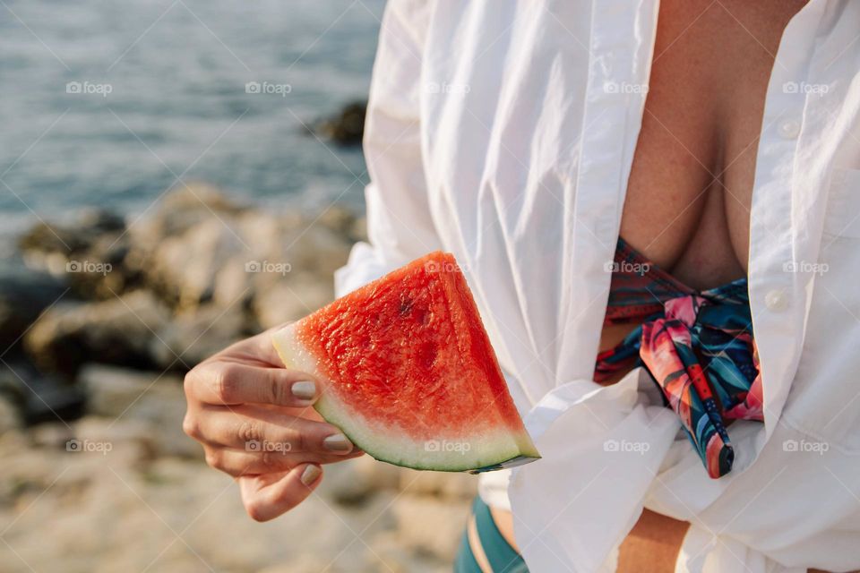 Close-up midsection  photo of woman on beach holding piece of watermelon