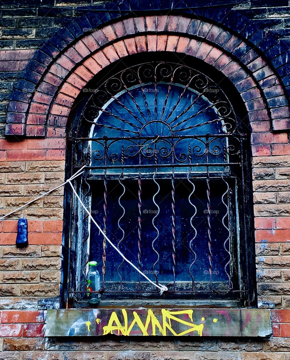 An 2nd floor arched window in Bklyn off Fulton St w iron cast ornamented bars in an abandoned building once built in the oldfashioned style of the turn of the century in the 1890s a.k.a. the „Victorian Age“. 2020. Hypnotic Productions