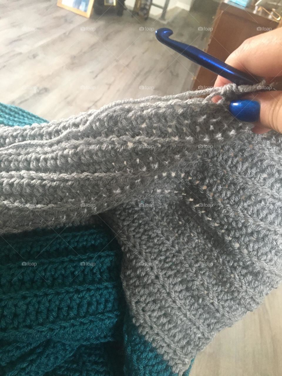 Creative middle aged lady, holds up her teal blue and grey afghan shes crochetting, with tips of thumb and pointer finger