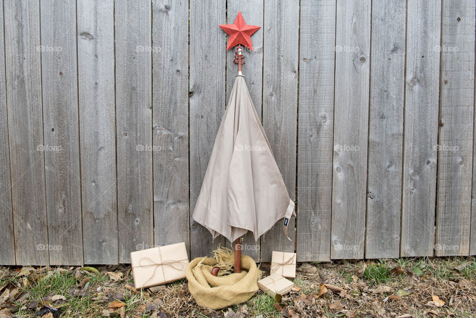 Umbrella with a star on top of it propped up against a wooden fence to look like a Christmas tree