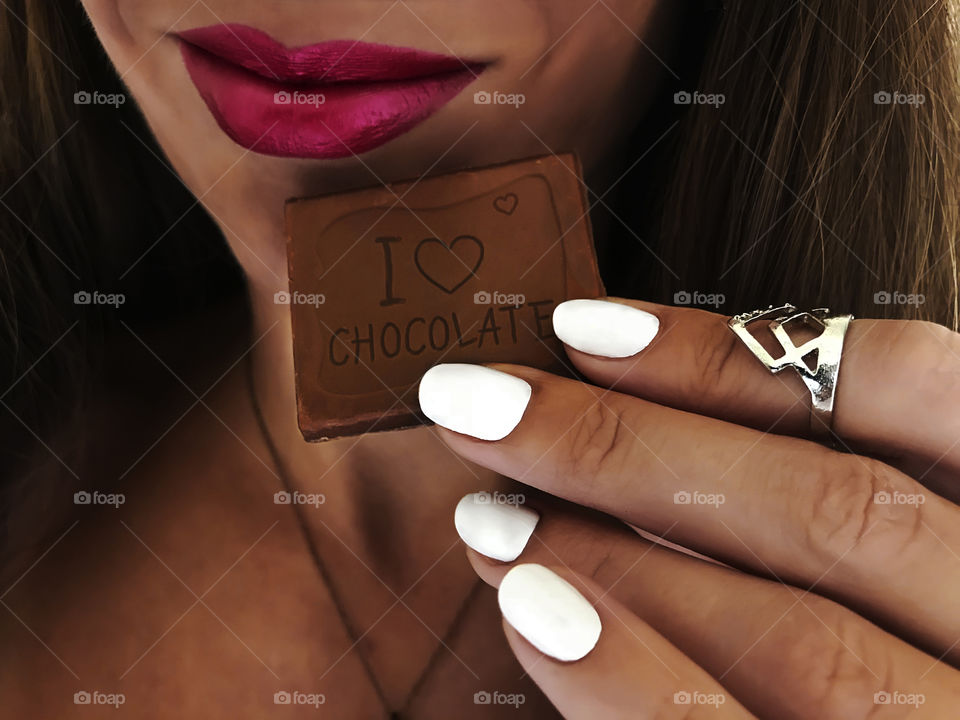 Young woman with beautiful white manicure happily having a bar of favorite chocolate 