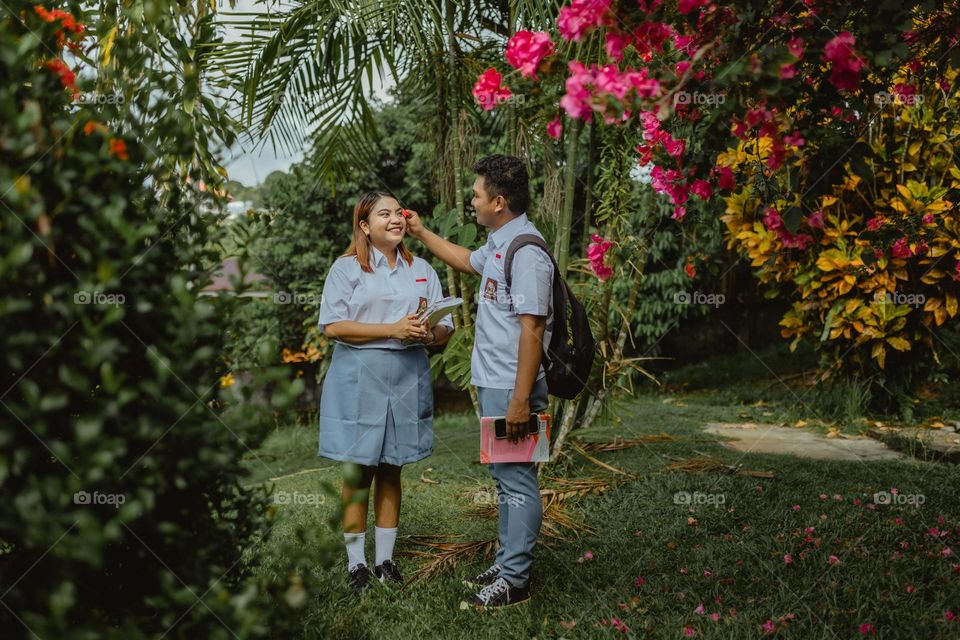 high school couple standing in park school with red flower blooms