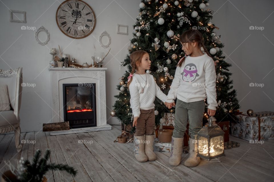 Little sisters near Christmas tree at home