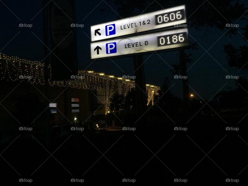 Directions leading to a car park in the mall just after dark.There are mall decorations in the background. The dark, parking sign and mall decorations bring out the contrast.