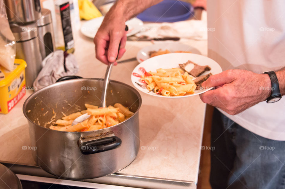 Man In The Kitchen Serving Penne Pasta Macaroni With Tomato Sauce And Meatloaf In A Plate
