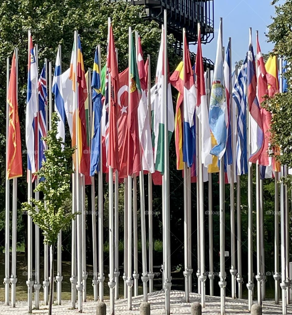 A vibrant display of flags from various nations, standing still in Munich, Germany. The flags, with their distinct colors and designs, are arranged in a row, creating a striking visual contrast, and symbolizing unity and international presence.