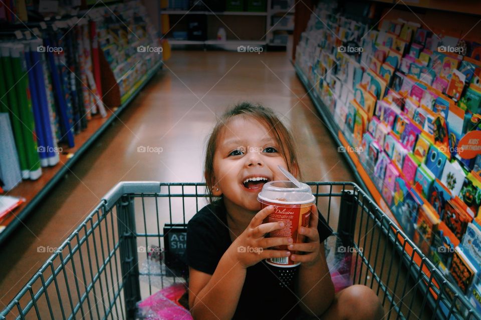 Little girl sitting on shopping cart in mall