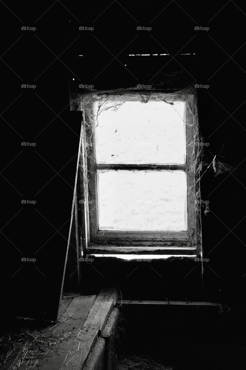 A cobweb-covered, hayloft window in an old, dusty barn in black-and-white