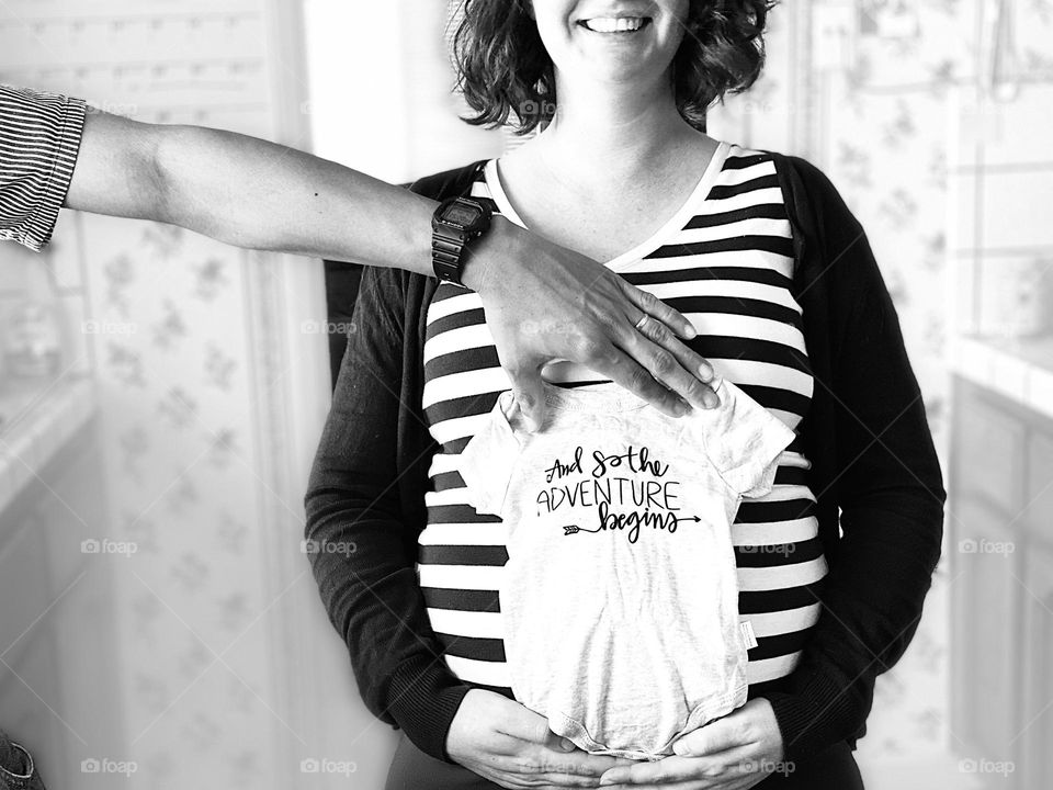 An expectant mother and the father hold a onesie against the mother’s baby bump