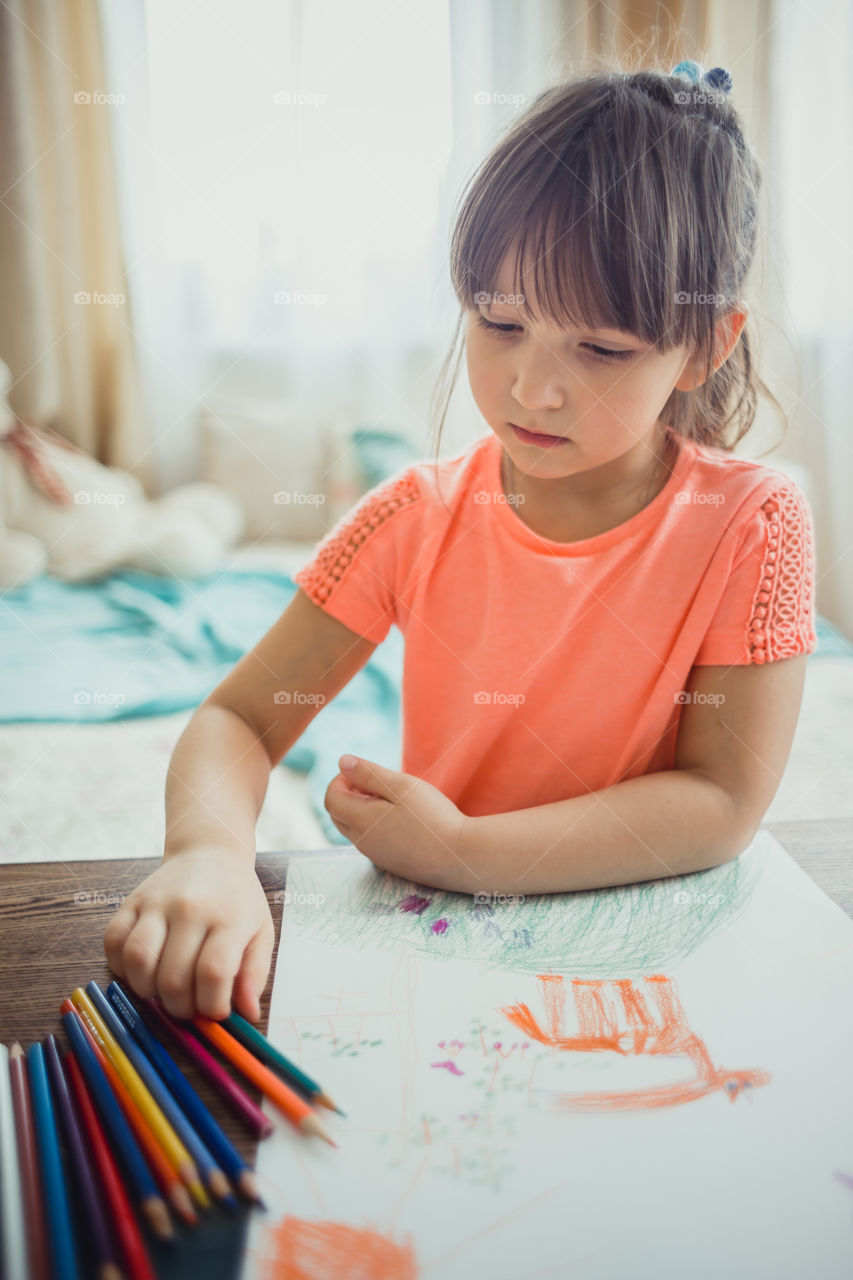 Little girl drawing with colorful pencils at wooden desk indoor