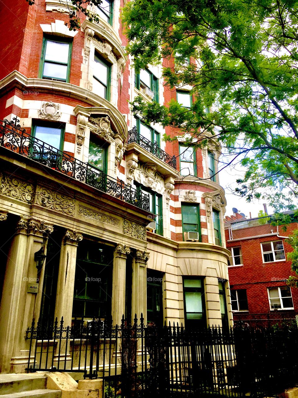 A Fort Greene, Bklyn brownstone w eclectic design featuring: ionic Greek style columns, offset levels w half round shapes, balconies w iron cast artful design on the railings, ornamented window frames, a striped facade. 2019. Hypnotic Productions