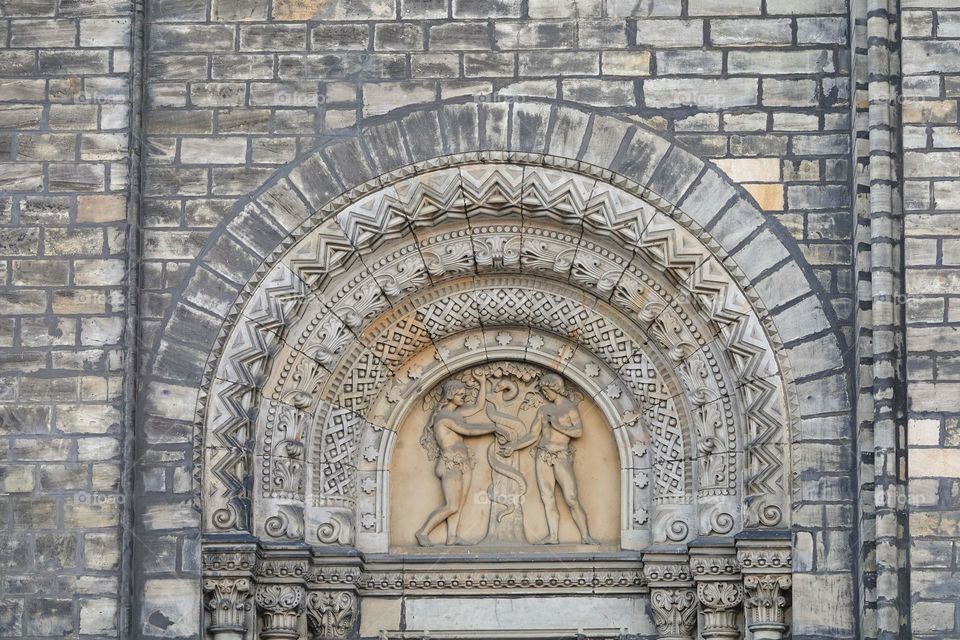 Relief with the Adam and Eve by tree of the knowledge of good and evil. Neo-romanesque portal of old Saint Cyril and Methodius Church from the 19th century in Karlin, Prague, Czech Republic.