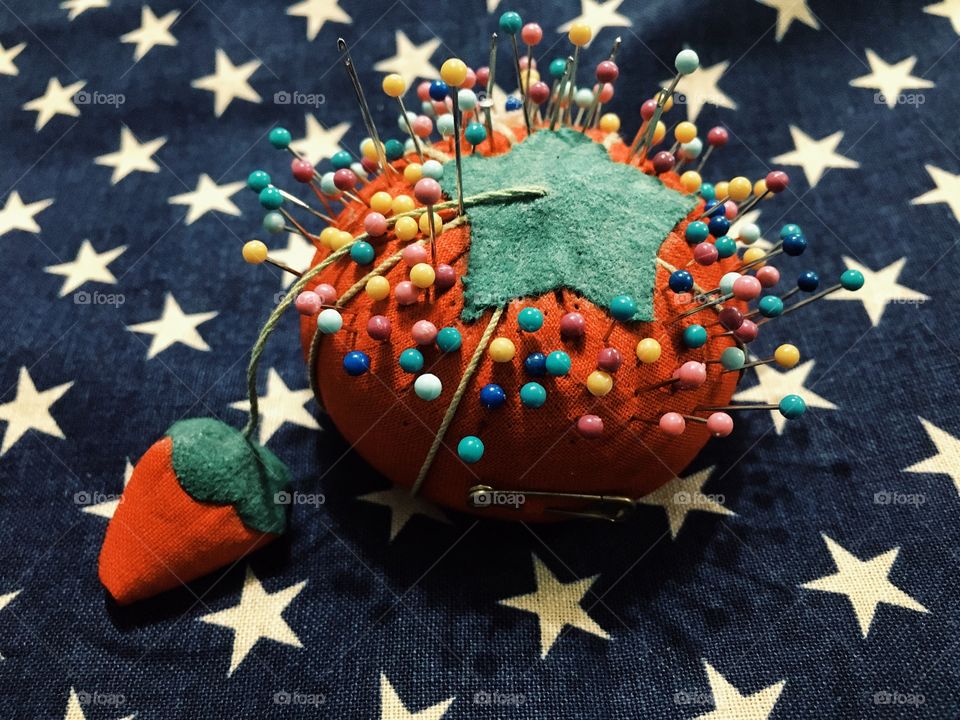 Pin cushion full of colorful sewing pins on top of a star pattern fabric 