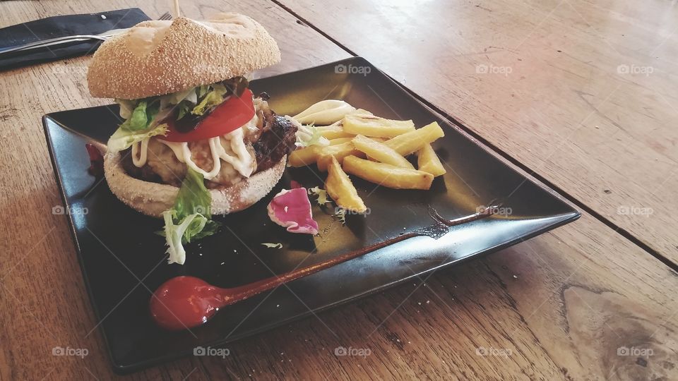 Tasty big burger with french fries on a wooden table of a restaurant